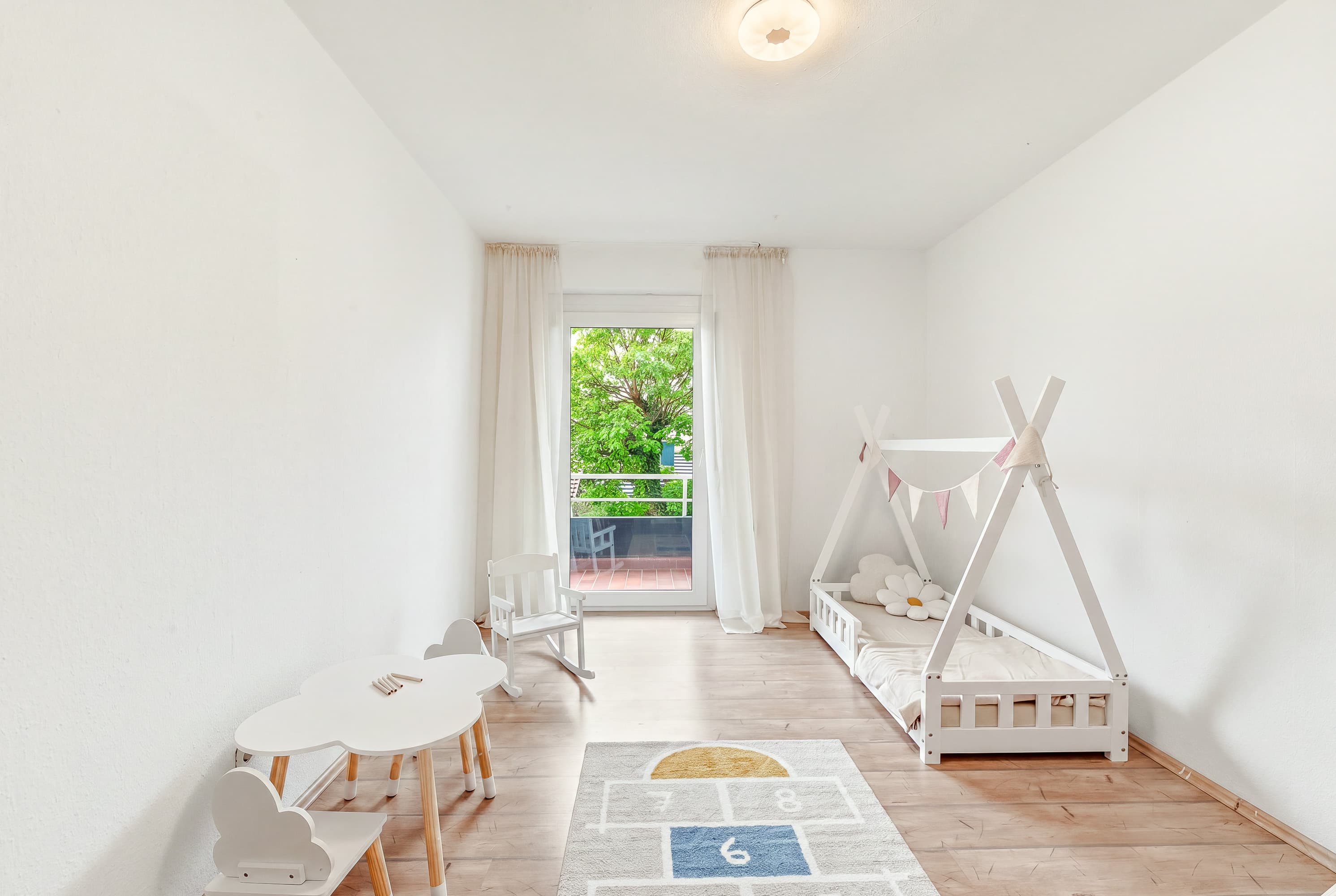 Kinderzimmer mit Spielzelt, Kindertisch und Zugang zum Balkon